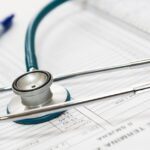 A stethoscope and pen resting on a medical report in a healthcare setting.