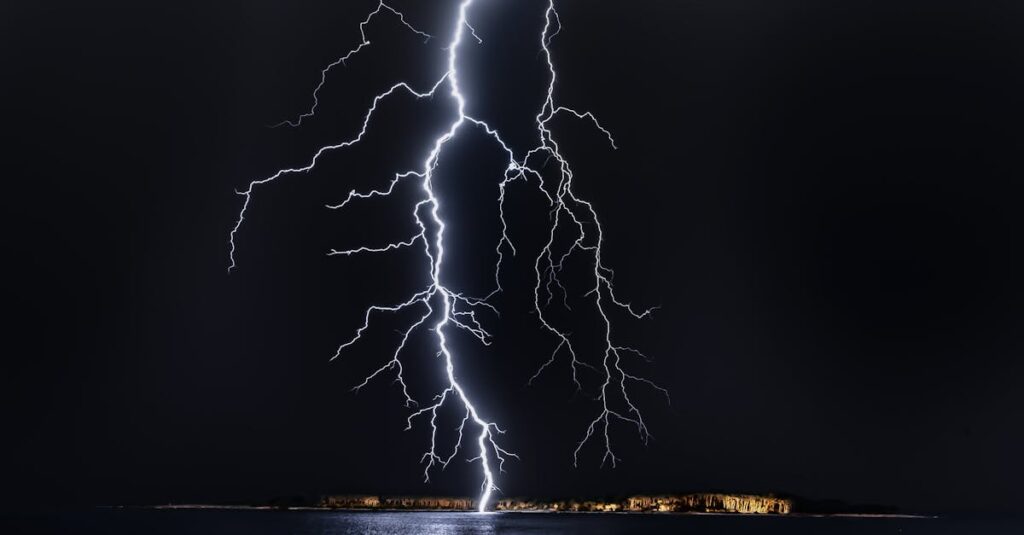 Dramatic lightning bolt over the ocean at night, illuminating the coastal landscape.