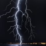 Dramatic lightning bolt over the ocean at night, illuminating the coastal landscape.