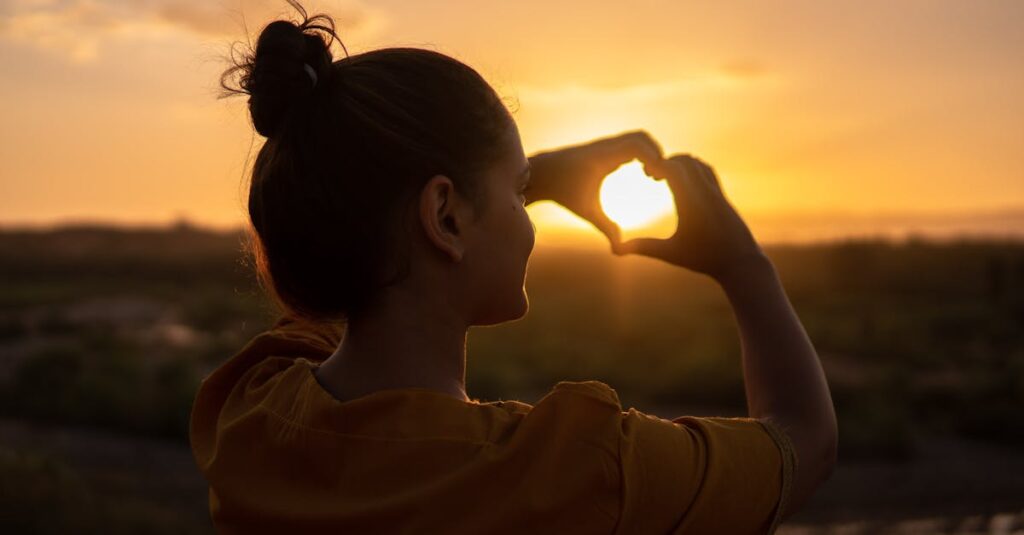 A silhouette of a young woman forming a heart shape at sunset in Kelâat M'Gouna, Morocco.