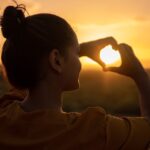 A silhouette of a young woman forming a heart shape at sunset in Kelâat M'Gouna, Morocco.