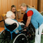 A caregiver talks with elderly women in a wheelchair at a retirement home.