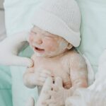 A newborn baby just delivered, attended by medical staff wearing gloves in a hospital setting.