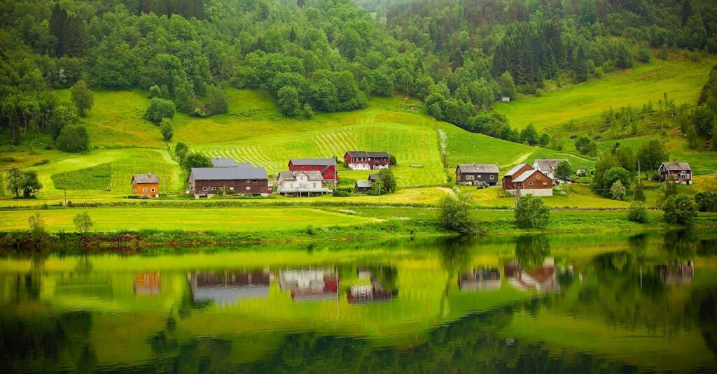Tranquil countryside scene with houses reflected in a calm river.