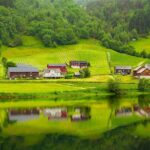 Tranquil countryside scene with houses reflected in a calm river.