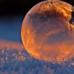 Close-up shot of a frozen bubble with warm reflections resting on a snowy surface at twilight.