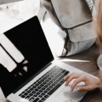 A young woman works remotely at a café, using her laptop and external hard drive.