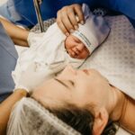 A mother cradling her newborn immediately after childbirth in a hospital setting.
