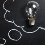 Light bulb laying on chalkboard with drawn thought bubble, symbolizing creative ideas.