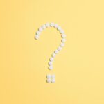 White pills arranged into a question mark shape on a vibrant yellow background.