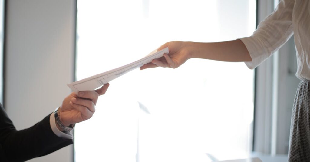 Close-up of hands exchanging documents in a business setting indoors.