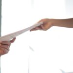 Close-up of hands exchanging documents in a business setting indoors.