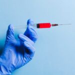 Close-up of a gloved hand holding a syringe with red fluid against a blue background, symbolizing healthcare and medicine.