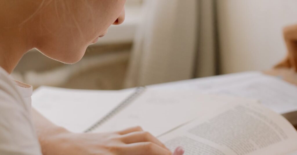 Focused young woman writing notes from an open textbook at a desk, creating a study environment.