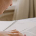 Focused young woman writing notes from an open textbook at a desk, creating a study environment.