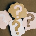 Four paper cutouts of question marks in beige and white on a brown surface, symbolizing inquiry and curiosity.