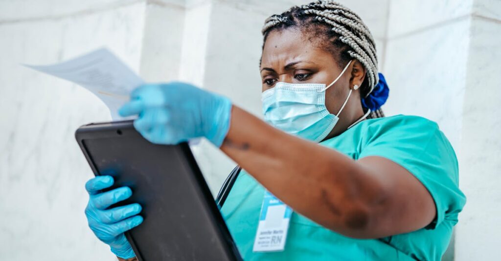 Low angle of focused black female nurse in mask and gloves standing in hospital and looking through papers