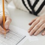 A student writing answers on a multiple-choice exam sheet at a desk.