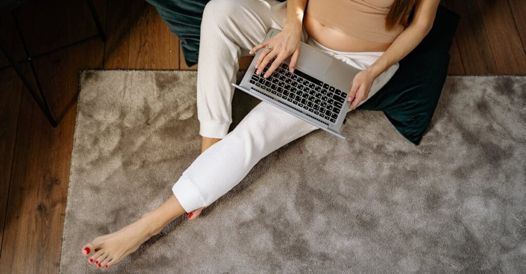 Pregnant woman sitting on carpet working remotely on laptop, enjoying a comfortable home environment.