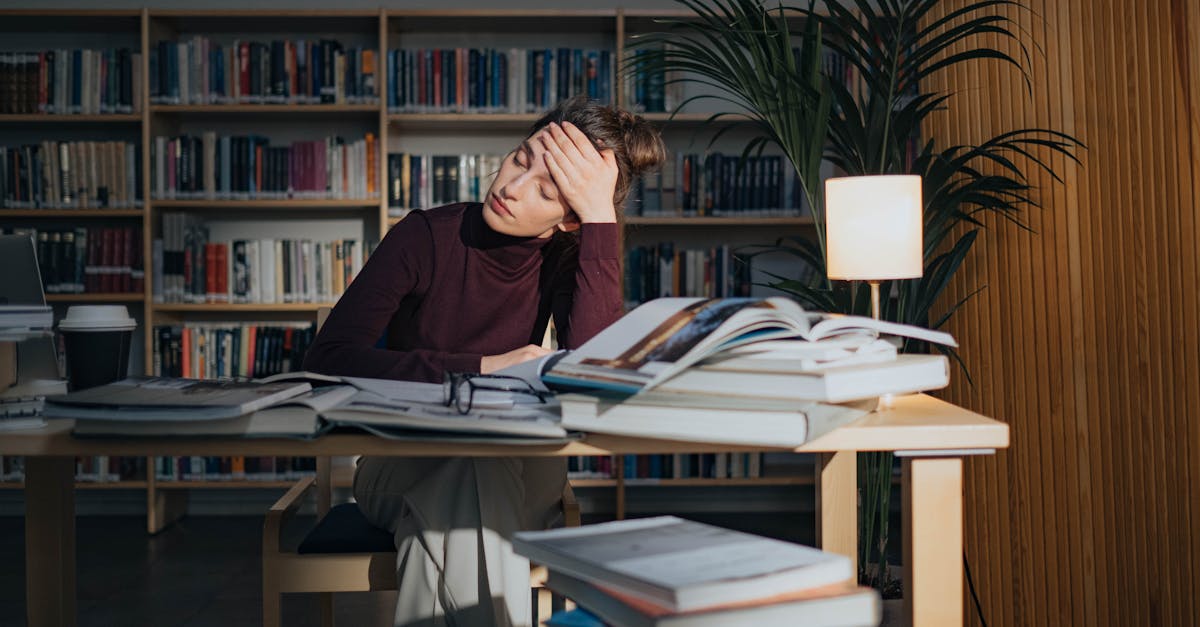 A tired woman surrounded by books, studying in a library, feeling overworked and stressed.