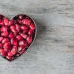 Delicious and juicy pomegranate seeds in a heart-shaped bowl on a wooden table.