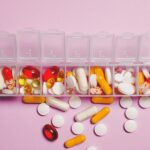 A variety of pills in a weekly pill organizer on a pink background.