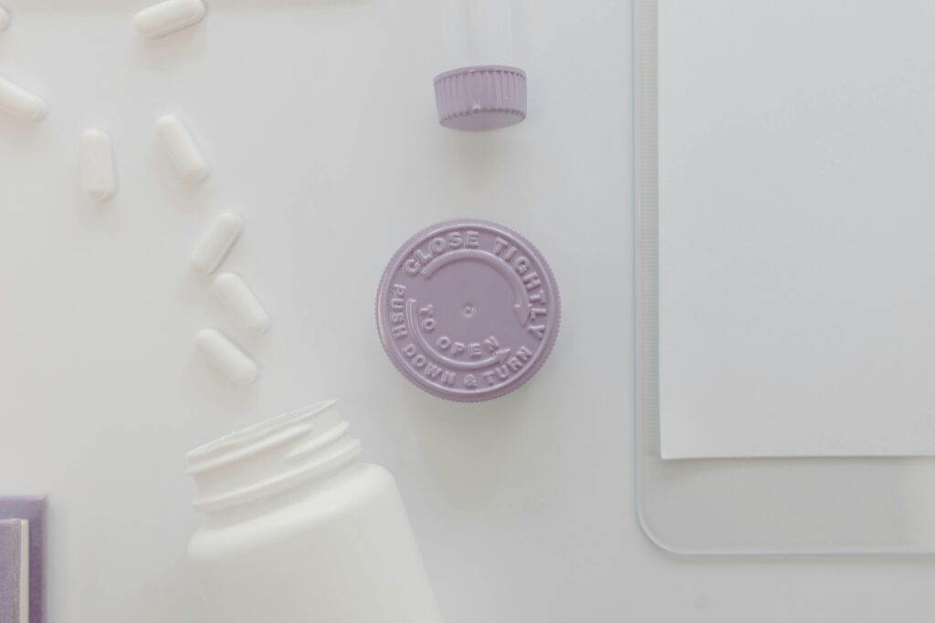 Minimalist flat lay of medicine bottles, pills, and a purple cap on a white surface.