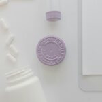 Minimalist flat lay of medicine bottles, pills, and a purple cap on a white surface.